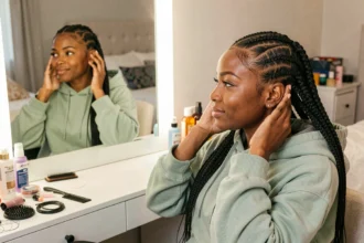 Jeune femme noire avec des nattes collées style célébrité devant un miroir de coiffeuse à la maison